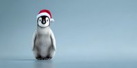 Adorable baby penguin wearing red Santa hat standing alone on light blue background, perfect for holiday greeting cards and winter designs.