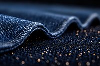 Close-up macro shot of dark blue denim fabric texture with wave pattern and water droplets creating sparkle effect against black background, showing textile detail.
