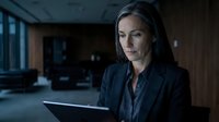 Middle-aged woman with long dark hair, Caucasian ethnicity, wearing dark business blazer, working on laptop in modern office environment at night, professional corporate setting.