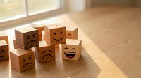 Wooden blocks with different emotional faces scattered on hardwood floor in bright sunlit room representing mood diversity and emotional intelligence concepts.