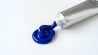 Blue paint squeezed from metal tube creating artistic swirl on white background. Professional art supplies for creative projects and design work.