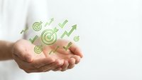 Businessman hand holding green growth icons with target, checkmarks and upward arrows symbolizing business success, profit increase and financial goals achievement.