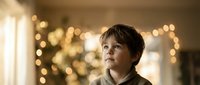 Young boy with brown hair gazing upward with wonder and curiosity in warm golden bokeh lighting creating magical atmosphere for holiday celebrations.