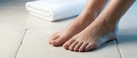 Female feet standing on clean white bathroom tiles next to folded towel, spa wellness hygiene concept for health and beauty care products.