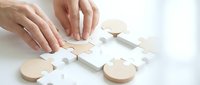 Woman's hands assembling wooden puzzle pieces on white surface, representing problem-solving, strategy, and business solutions for corporate training and educational materials.
