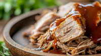 Tender slow-cooked pulled pork with rich barbecue sauce served in rustic wooden bowl, perfect for comfort food recipes and restaurant menu photography.