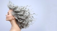 Mature woman with long flowing silver hair in profile against neutral background, representing aging, beauty and natural hair care for mature demographics.