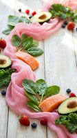 Fresh salmon fillet with avocado, spinach leaves, kale and mixed berries on pink fabric over rustic white wooden background for healthy eating concepts.