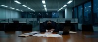 Exhausted businessman with head in hands at conference table surrounded by paperwork in modern office during late night work session.