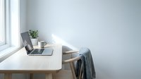 Minimalist home office workspace with laptop, coffee cup and plant on wooden desk by window. Clean modern interior design for remote work and productivity.