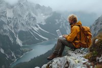 Digital nomad working remotely on mountain peak overlooking turquoise alpine lake, wearing yellow jacket and backpack. Perfect for travel, lifestyle and remote work concepts.