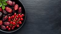 Fresh cranberries and dried dates in black bowl on dark slate background. Healthy antioxidant-rich superfood ingredients for cooking and baking recipes.
