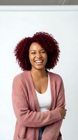 Happy African American woman with burgundy curly hair laughing in pink cardigan sweater against white background for lifestyle and portrait projects.