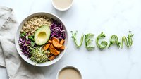 Fresh vegan bowl with quinoa, avocado, red cabbage, sweet potato, and sprouts on marble, with word Vegan made of microgreens beside it.