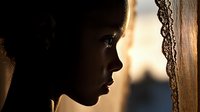 Silhouette profile of young African woman near window with lace curtain at sunset, dramatic lighting creates mysterious atmospheric mood for portraiture and storytelling.