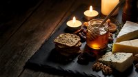 Artisanal cheese platter with honey jar, crackers, nuts and candles on dark slate board creating cozy evening atmosphere for gourmet dining and entertaining.