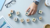 Hand selecting wooden eco-friendly icons on desk with glasses and coffee. Sustainable business concept for environmental marketing and green choices.