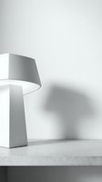 Modern table lamp with conical shade casting soft shadow on white wall, positioned on concrete surface for contemporary interior design and home decor projects.