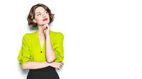 Young woman with short wavy hair in bright lime green blouse and black skirt looking up thoughtfully against white background, professional portrait for business content.