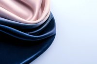 Luxurious silk fabric waves in navy blue and blush pink colors on white background, creating elegant flowing curves and soft folds with dramatic lighting effect.