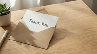Thank you card tucked in a kraft paper envelope on a wooden desk with a pen and small plant, conveying gratitude and appreciation.