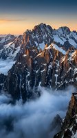 Dramatic snow-capped mountain peaks rising above clouds during golden hour sunrise with warm light illuminating rocky cliffs and misty valleys below.