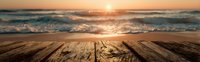 Rustic wooden deck overlooking ocean waves at sunset, golden light reflecting on water surface.