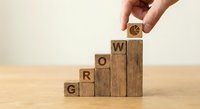Hand placing wooden blocks spelling GROW in ascending steps on wooden surface, business growth and development concept for presentations and marketing.