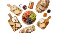 Assorted cheese, fresh fruits, bread, and preserves arranged on wooden boards and white background, ready for gourmet food styling and culinary content.