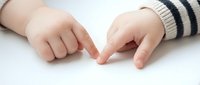Infant hands touching together on white surface, wearing striped sleeve, closeup of baby fingers and palms for parenting and childcare content.