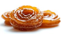 Golden spiral jalebi sweets with crystallized sugar coating on white background. Traditional Indian dessert pastry in coiled shape for festive celebrations.