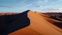 Dramatic sand dune ridge in desert landscape with sharp contrast between sunlit and shadowed sides, sweeping curves against blue sky with wispy clouds at sunset.