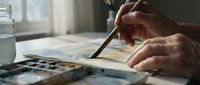 Artist hands painting watercolor artwork with brush and palette creating colorful abstract composition on paper in natural light studio workspace.