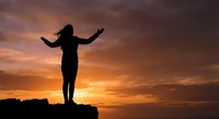 Woman silhouette with raised arms celebrating freedom and success against dramatic sunset sky. Concept of achievement, motivation and personal growth.