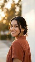 Young Hispanic woman smiling warmly in golden hour sunlight wearing rust colored shirt with soft bokeh background for lifestyle and portrait photography.
