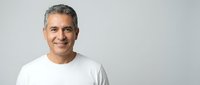 Middle-aged Hispanic man with gray hair smiling confidently in white t-shirt against neutral background for lifestyle and portrait photography.