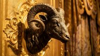 Ornate bronze goat head sculpture mounted on golden decorative wall panel with baroque scrollwork details, suitable for luxury interior design and architectural decoration projects.