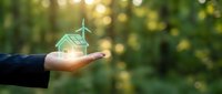 Businessman holding glowing green eco house with solar panels and wind turbine, sustainable energy concept on nature bokeh background.