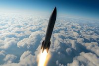 Rocket soaring through stratosphere above white clouds with bright engine flame, dramatic low angle view against blue sky horizon. For aerospace and space exploration concepts.
