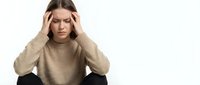 Young Caucasian woman in beige sweater holding head with both hands expressing stress, headache or mental fatigue against white background.