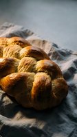 Fresh baked challah bread loaf with golden brown crust on linen cloth, traditional Jewish braided bread for Shabbat dinner and holidays.