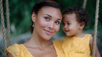 Young Asian mother and mixed race toddler in matching yellow outfits share joyful moment on swing outdoors, expressing genuine happiness and family bonding.