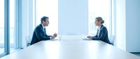 Professional business meeting with male and female executives discussing strategy at modern conference table in bright office with large windows.