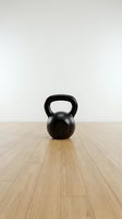 Black kettlebell weight on wooden gym floor against white wall background. Strength training equipment for fitness workouts and home exercise routines.