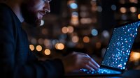 Bearded man working on laptop at night with glowing screen and bokeh lights in background, creating atmospheric business environment for remote work concept.