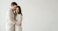 Happy couple in matching beige linen outfits embracing intimately against neutral background for lifestyle and relationship content.