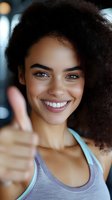 Happy young African American woman giving thumbs up gesture with bright smile in fitness setting for motivation and success concepts.