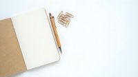 Open notebook with wooden pen and paper clips on white background for office workspace and writing projects.