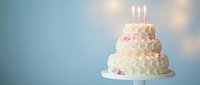 White three-tier wedding cake with pink roses and lit candles on blue background for celebration and special occasions.