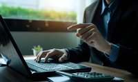 Professional businessman working on laptop computer at modern office desk with natural sunlight streaming through window creating productive workspace atmosphere.